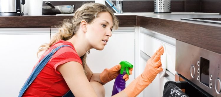 Young woman cleaning kitchen cabinets with a spray cleaner.