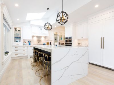 Bright and spacious modern white kitchen featuring a large marble island with gold bar stools and stylish geometric pendant lights.