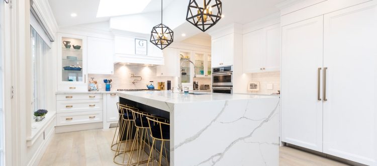 Bright and spacious modern white kitchen featuring a large marble island with gold bar stools and stylish geometric pendant lights.