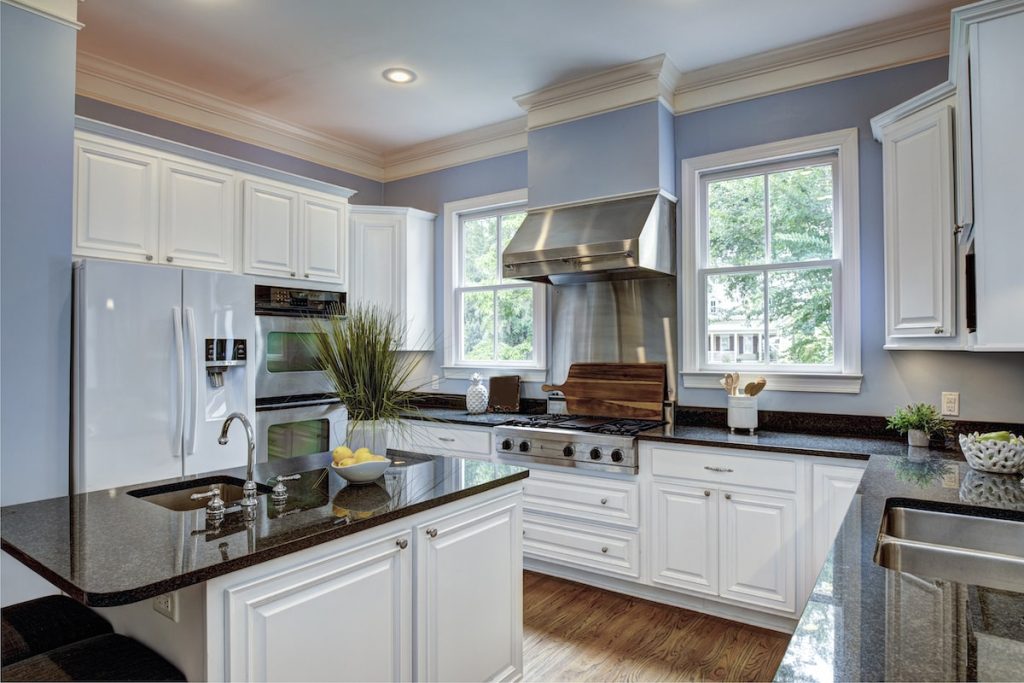 Elegant kitchen with white cabinets, granite countertops, and stainless steel appliances. Featuring a center island, large windows, and hardwood flooring.