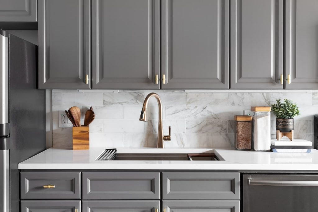 A contemporary kitchen featuring elegant gray cabinets, a marble backsplash, and a sleek faucet, combining functionality with stylish design elements.