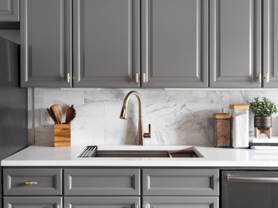 A contemporary kitchen featuring elegant gray cabinets, a marble backsplash, and a sleek faucet, combining functionality with stylish design elements.