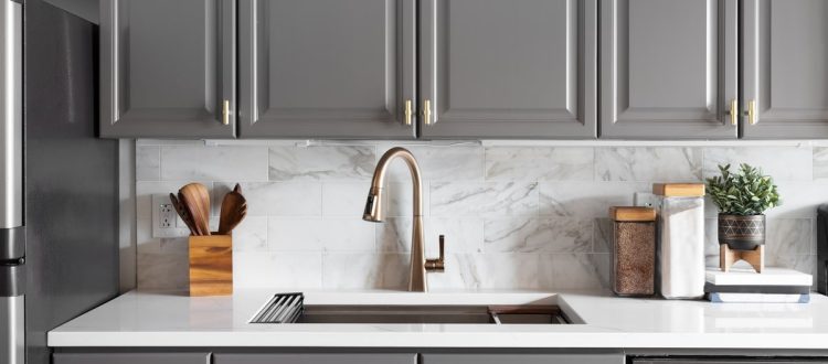 A contemporary kitchen featuring elegant gray cabinets, a marble backsplash, and a sleek faucet, combining functionality with stylish design elements.