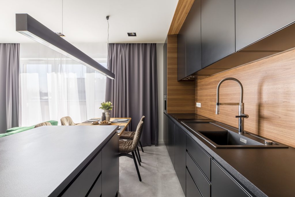 A sleek, modern kitchen featuring black cabinets, wood accents, and a stylish dining area with natural light from large windows, creating a sophisticated and inviting space.