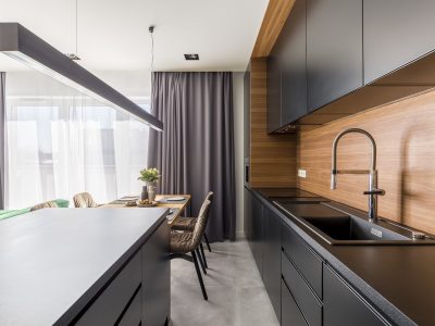 A sleek, modern kitchen featuring black cabinets, wood accents, and a stylish dining area with natural light from large windows, creating a sophisticated and inviting space.