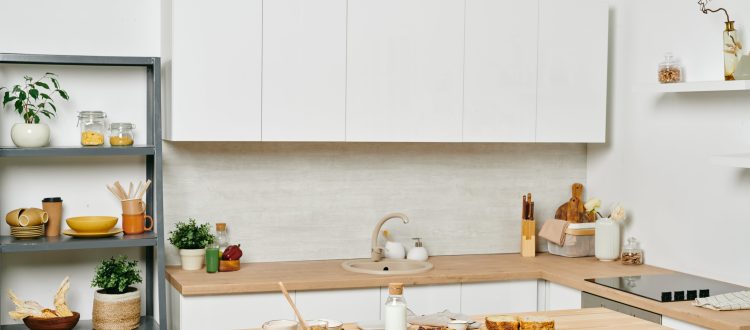 A clean and minimalist kitchen featuring white cabinets, wooden countertops, and open shelving with neatly arranged kitchenware, creating a stylish and functional space.