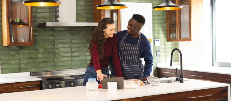 A cheerful couple enjoying cooking together in a stylish modern kitchen with wooden cabinets and pendant lights, creating a warm and inviting atmosphere.