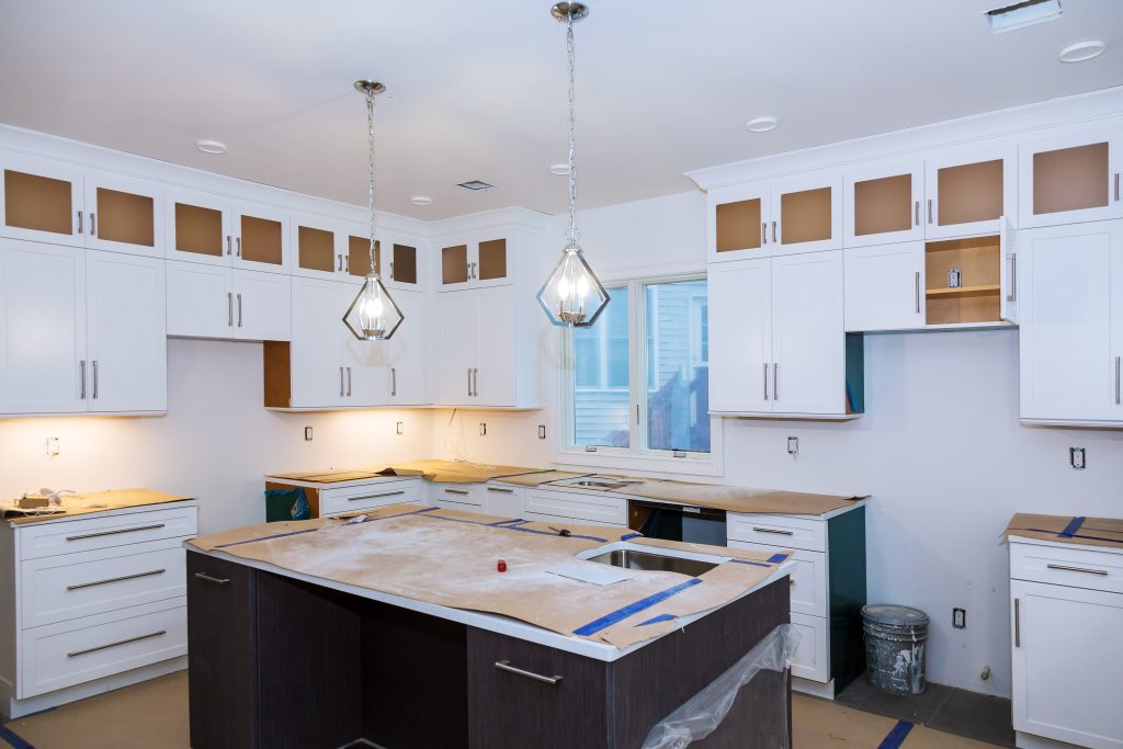 A modern kitchen in the midst of renovation, featuring new white cabinets, pendant lights, and a large island, ready for finishing touches.