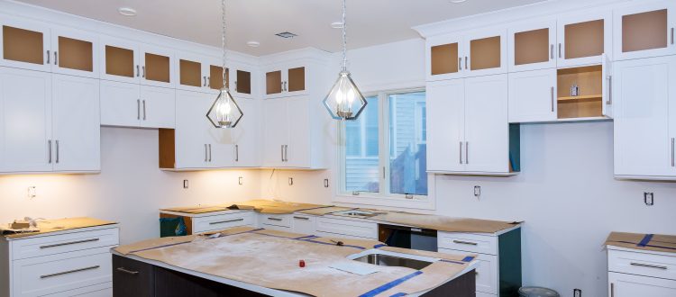 A modern kitchen in the midst of renovation, featuring new white cabinets, pendant lights, and a large island, ready for finishing touches.