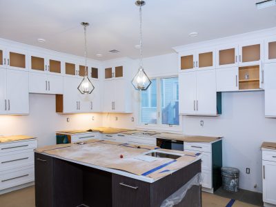 A modern kitchen undergoing renovation, featuring newly installed white cabinets and pendant lights, creating a bright and updated space.