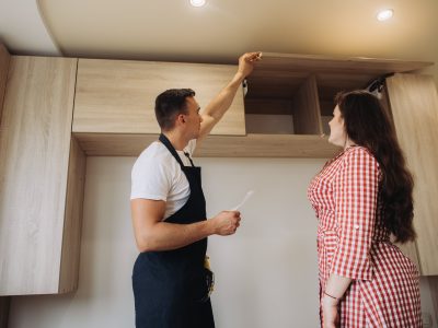 A man and a woman discussing kitchen renovations, with the man showing the new cabinet installations and explaining details.