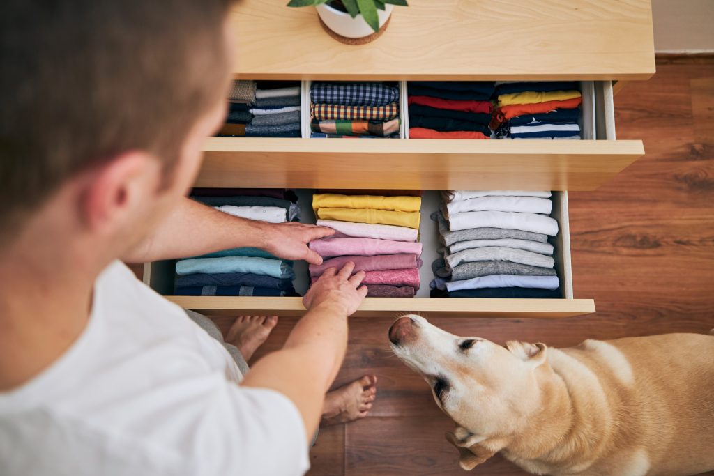 Man folding clothes in drawer with dog nearby