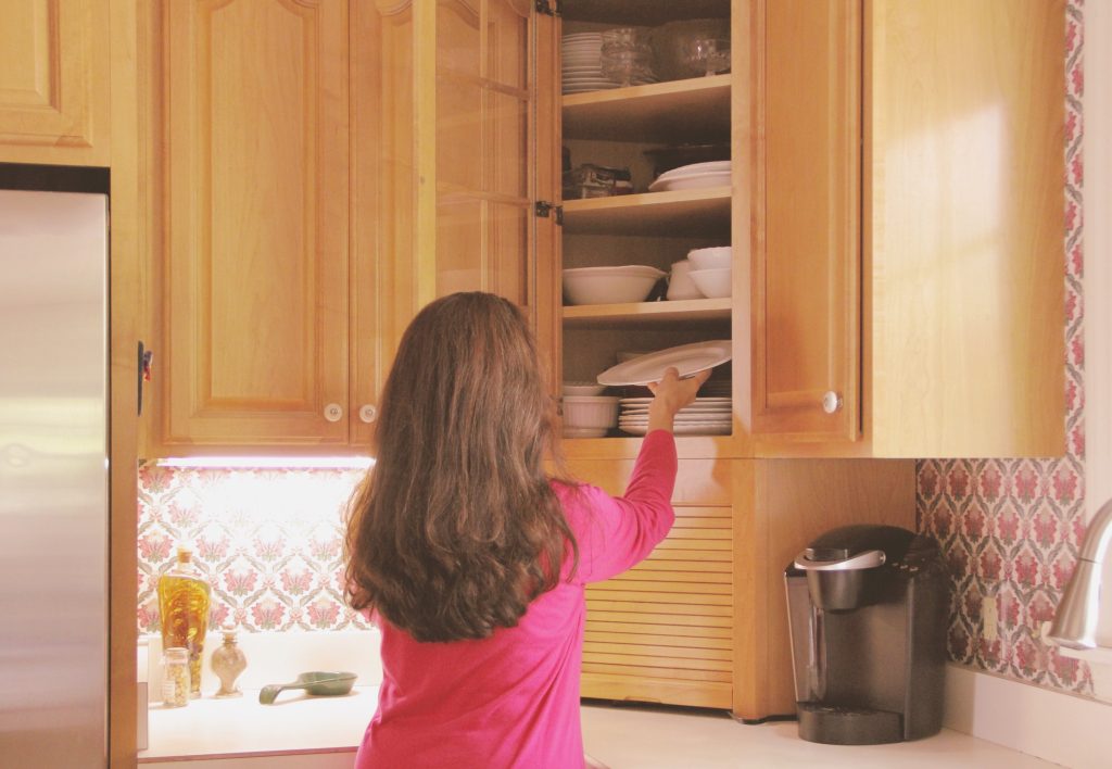 Woman placing plate in kitchen cabinet